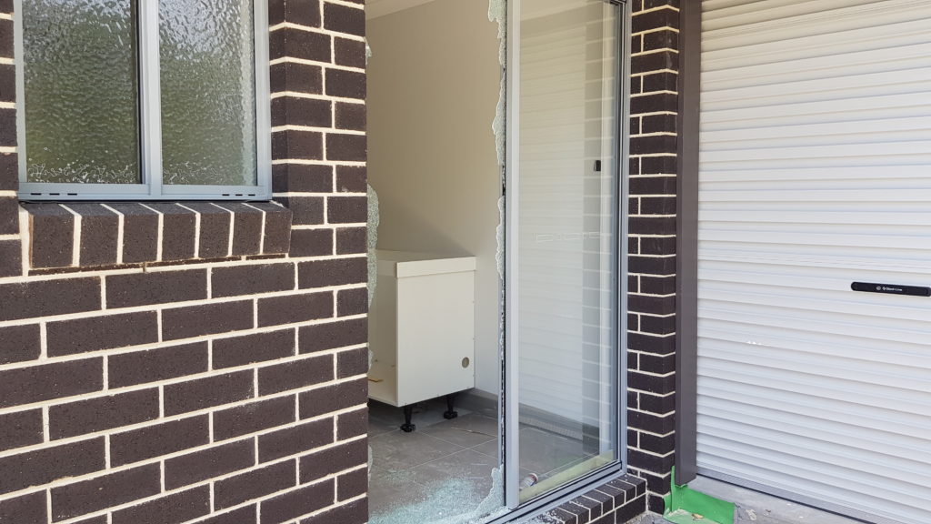 new house under construction with brown bricks with white grout. The sliding door has been smashed by vandals